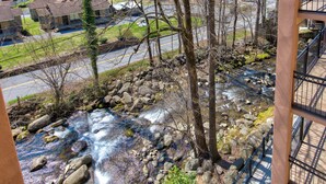 Vista de un río con rocas y árboles, una carretera y un edificio con balcón.