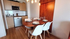 A compact kitchen with modern appliances, a dining table set for four, and white chairs. - T2 swimming pool, terrace, private parking R. Pic du Midi (Bagnères-de-Bigorre)