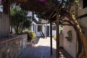 A brick pathway leading to a white building with a covered area and two Adirondack chairs.