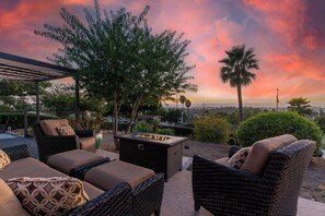 An outdoor seating area with wicker furniture and a fire feature, overlooking a scenic landscape.