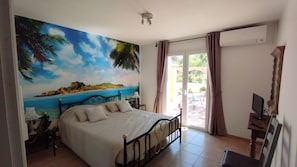 A bedroom with a bed, a desk with a computer, a window with curtains, and a mural of a beach scene. - Les Palmiers – Sleeps 6, with a pool and air conditioning (Trans-en-Provence)