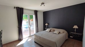 A bedroom with a bed, two bedside lamps, a ceiling fan, and a sliding glass door leading to an outdoor area. - Les Palmiers – Sleeps 6, with a pool and air conditioning (Trans-en-Provence)