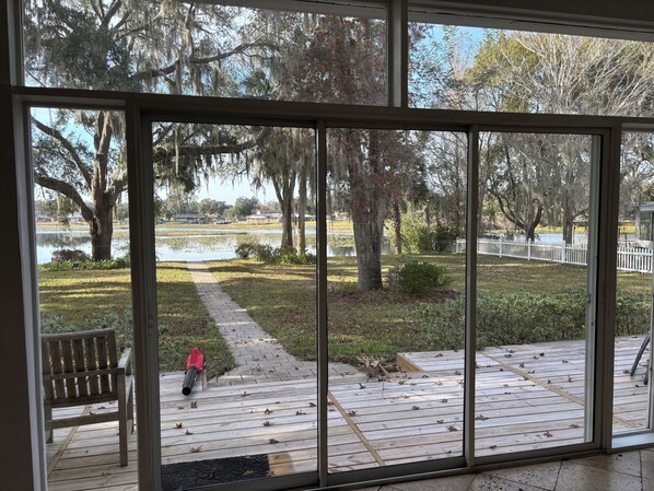 A view through large windows of a deck with a wooden floor, a bench, and a red object on the deck. - Beautiful 4/2, 3000sf home on magnificent 430 A freshwater lake, family friendly (Inverness)