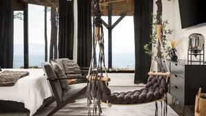 A modern bedroom with a large bed, a hanging chair, and a view of the ocean. - Monte Vista~Golf~Views~PS5~Sport Court~EV Charger (Berkeley Springs)