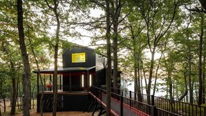 A secluded cabin with a wooden deck and a red railing, surrounded by trees. - Monte Vista~Golf~Views~PS5~Sport Court~EV Charger (Berkeley Springs)