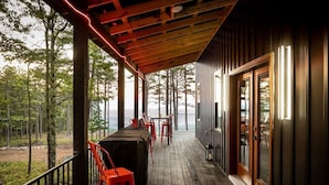 A wooden deck with a covered area, red chairs, and a view of a forest. - Monte Vista~Golf~Views~PS5~Sport Court~EV Charger (Berkeley Springs)