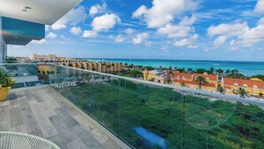 Un balcón con barandilla de vidrio que da a la costa, con edificios y cielo despejado.