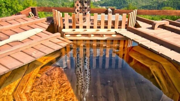 Um deck de madeira com superfície refletora, cercado por uma vedação de madeira e uma árvore.