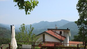 Um terraço com mesas ao ar livre, vista para montanhas e um edifício com telhado vermelho.
