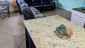 A living room with a black leather sofa, a dining table with a woven basket, and a ceiling fan. - Steps to Beach - Spacious 2BR + Arcade & Resort Backyard (Cocoa Beach)