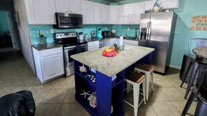 A kitchen with white cabinets, a blue island, stainless steel appliances, and a teal backsplash. - Steps to Beach - Spacious 2BR + Arcade & Resort Backyard (Cocoa Beach)