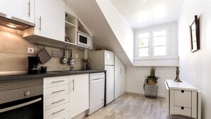 Una cocina moderna con armarios blancos, encimera negra y horno empotrado. Hay una ventana que proporciona luz natural y una planta en maceta en el suelo.