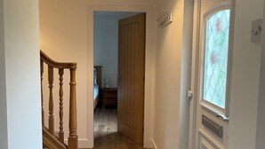 A hallway with wooden flooring, a wooden staircase, a door with a window, and a hanging light fixture. - Coorie Cottage, a peaceful Highland retreat for 6. Near Glencoe and Fort William (Fort William)