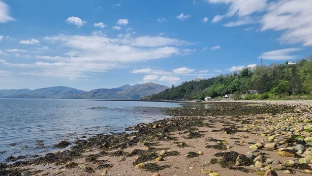 A beach with rocky shore, calm water, and mountains in the background. - Coorie Cottage, a peaceful Highland retreat for 6. Near Glencoe and Fort William (Fort William)