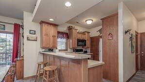 A kitchen with wooden cabinets, a bar area with stools, a microwave, and a refrigerator.