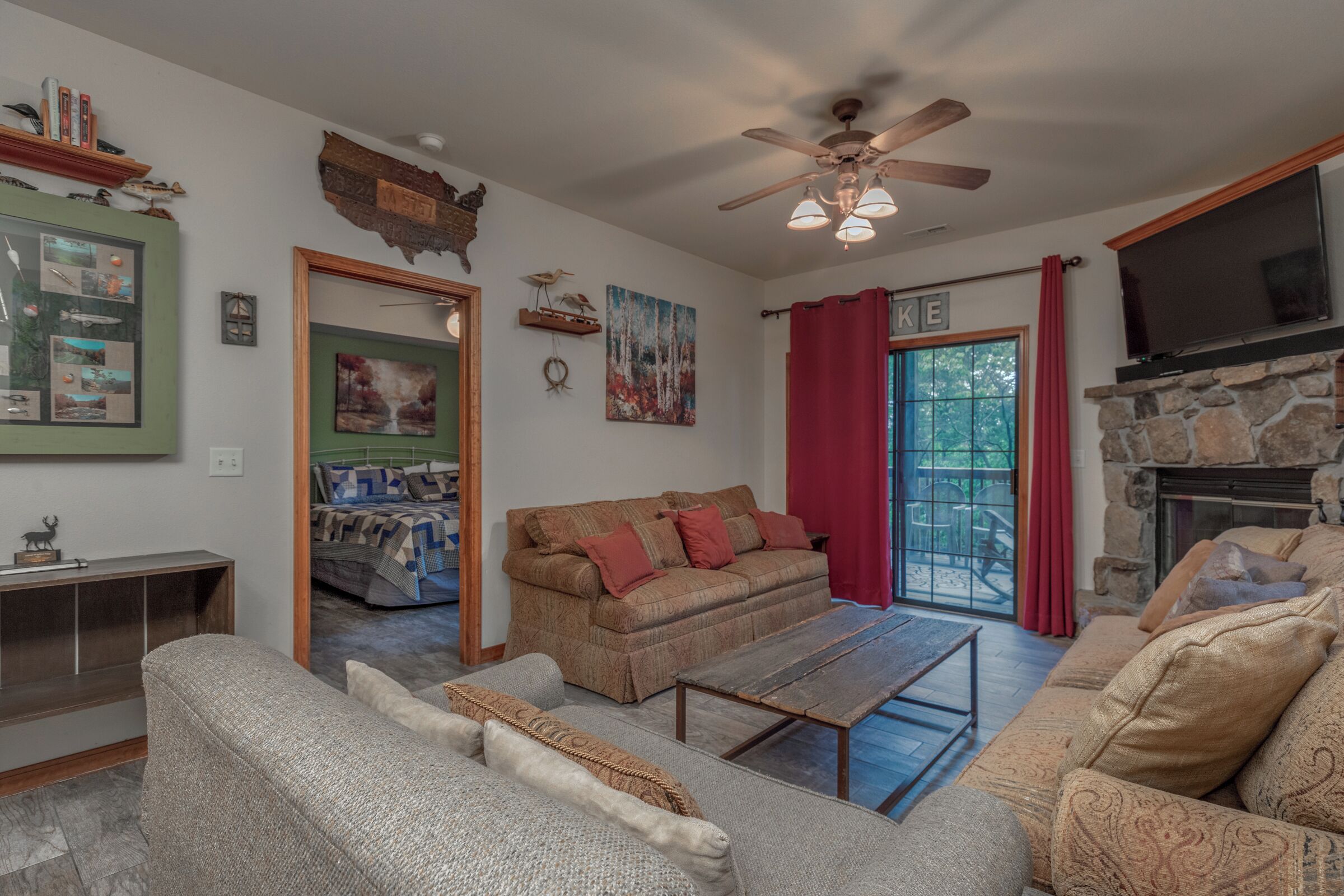 A cozy living room with a sofa, a coffee table, and a fireplace. There is a ceiling fan and a TV mounted on the wall.