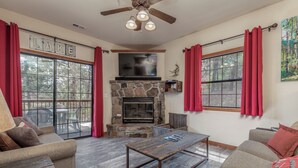 A living room with a stone fireplace, red curtains, and a ceiling fan.