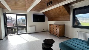 A spacious living area with a high ceiling, wooden beams, a large sofa, a coffee table, and a TV mounted on the wall. - Orchard Villa - Loft Apartment (Bled)