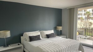 Moderni hotellihuone, jossa on suuri sänky, kaksi yöpöytää, lamppu ja näkymä ulkopuolella olevalle parvekkeelle.