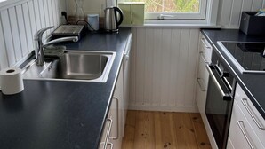 Eine kleine Küche mit Spüle, Herd und Fenster mit Blick auf ein Feld.