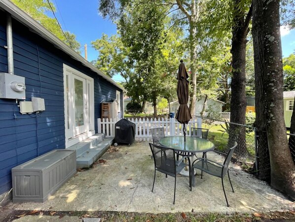 A blue house with a covered patio, a white picket fence, and a glass table with metal chairs.