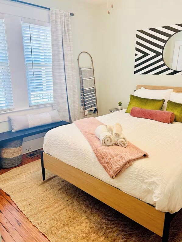 A neatly made bed with rolled towels, a wooden headboard, and a large mirror on the wall. - Blue Bungalow~Charming Carolina Place~Mins to Riverfront + UNCW~7 miles to Beach (Wilmington)