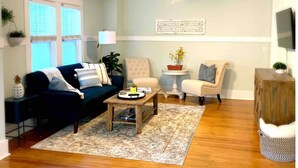 A living room with a dark blue sofa, a beige armchair, a wooden coffee table, and a patterned rug.
