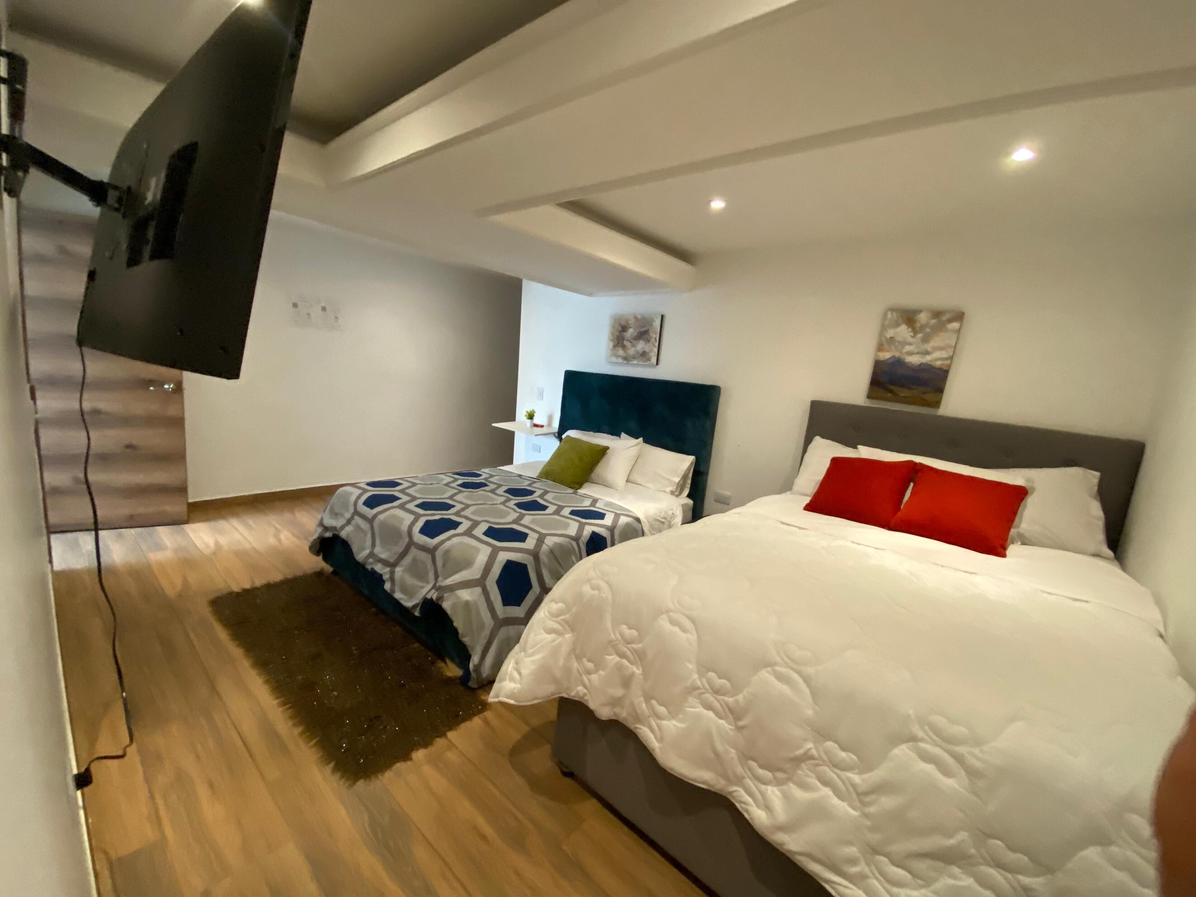 Een moderne hotelkamer met twee bedden, een wandgemonteerde flatscreen televisie en een houten vloer.