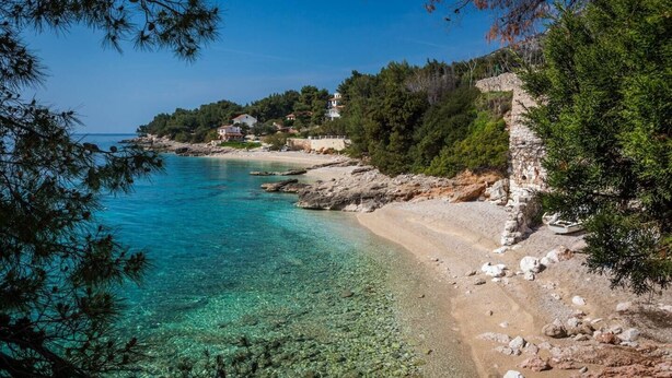 A coastal area with clear turquoise waters, rocky shoreline, and houses built on the hillside.
