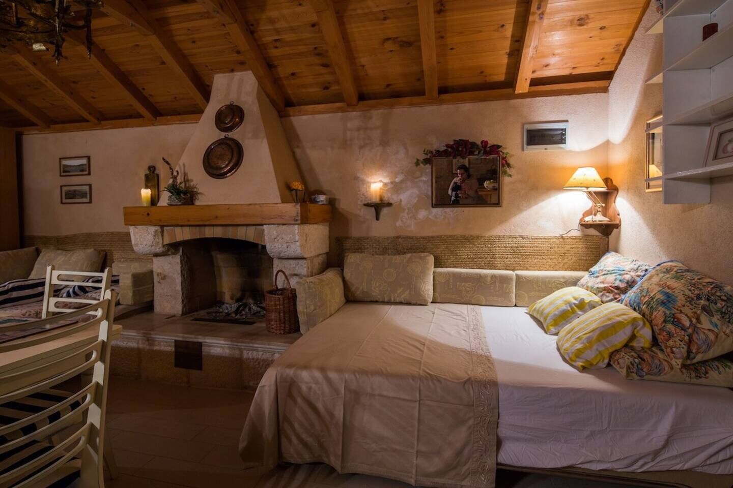 Une pièce chaleureuse avec une cheminée en pierre, un lit recouvert d’une literie à motifs floraux et un plafond en bois.