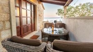 A cozy outdoor seating area with wicker furniture, a round table with wine glasses, and a bottle.
