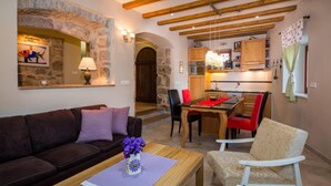 Un accogliente soggiorno con parete in pietra, travi in legno, zona pranzo con tovaglia rossa e cucina sullo sfondo.