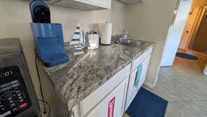 A kitchen with white cabinets, a coffee maker, a small sailboat model, and a sink.
