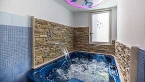 A bathroom with a stone wall, a window, and a bathtub with running water. - De Vivo Realty - Blue Angel Relais (Meta)