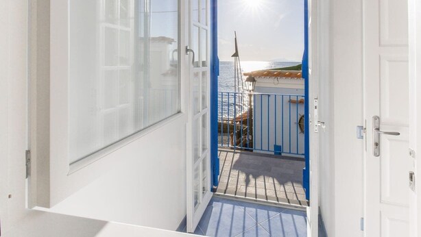 A narrow hallway with a glass door leading to a balcony with a blue railing. - De Vivo Realty - Blue Angel Relais (Meta)