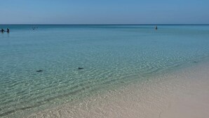 Una playa con aguas claras y poco profundas y una orilla arenosa.