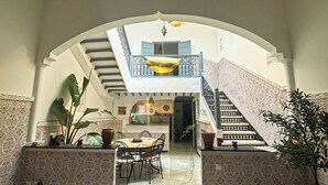 A dining area with a staircase leading to a balcony, surrounded by patterned walls and potted plants. - 10 minutes from the Majorelle garden Riad Beldi Chic An Authentic Stay”- Abritel (Marrakech)