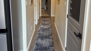A hallway with a patterned rug, a refrigerator, and a door with a chalkboard listing days of the week.
