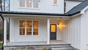 A two-story house with a front porch, a large window, and a door with a light fixture. - Newly built 4BR, close to Duke, ready for Duke Graduation! (Durham)