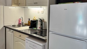 Een compacte keuken met witte kasten, een ingebouwde vaatwasser, een koelkast en een magnetron.