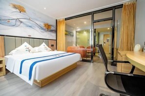Quarto de hotel com cama, escrivaninha e cadeira. Há uma porta de vidro que dá para uma varanda.
