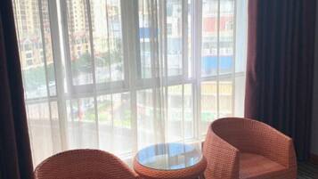Una habitación con dos sillones de mimbre y una mesita, ventanas amplias con vistas a edificios y una carretera.