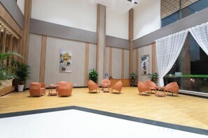 Un vestíbulo amplio con techos altos, un área de descanso central con sillas y plantas en macetas.