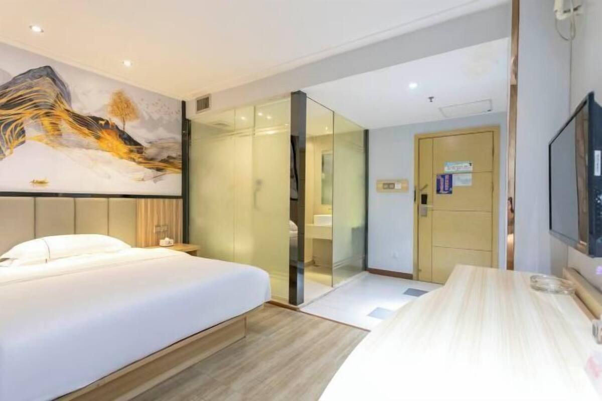 Une chambre d’hôtel moderne avec un lit, une télévision, une cloison en verre et un tableau au mur.