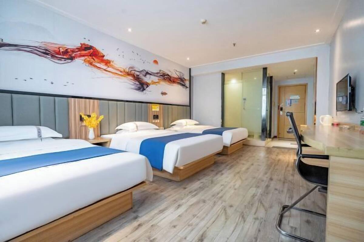 Une chambre d’hôtel avec trois lits, un bureau et une peinture abstraite moderne accrochée au mur.