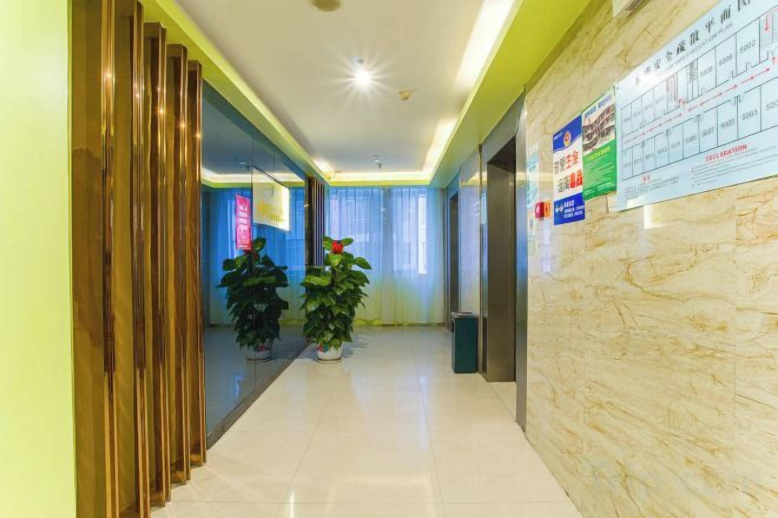 Un pasillo de hotel con mostrador de recepción, plantas en macetas y un tablón de anuncios con información.