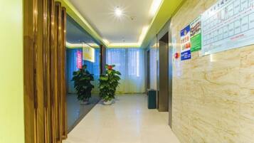 Un pasillo de hotel con mostrador de recepción, plantas en macetas y un tablón de anuncios con información.