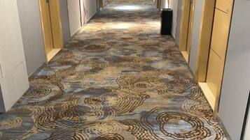 A carpeted hallway with a patterned design, leading to a room with a door at the end.