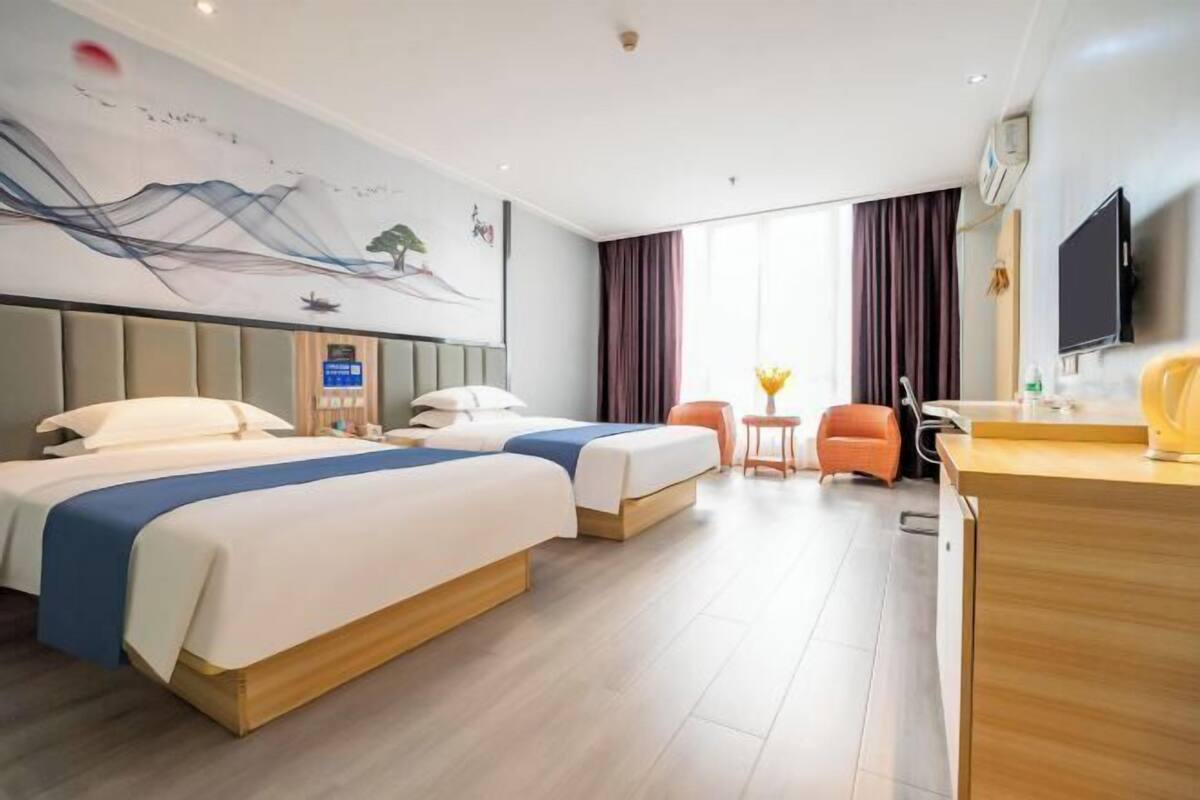 Une chambre d’hôtel avec deux lits, un bureau, une chaise, une télévision et un tableau au mur.