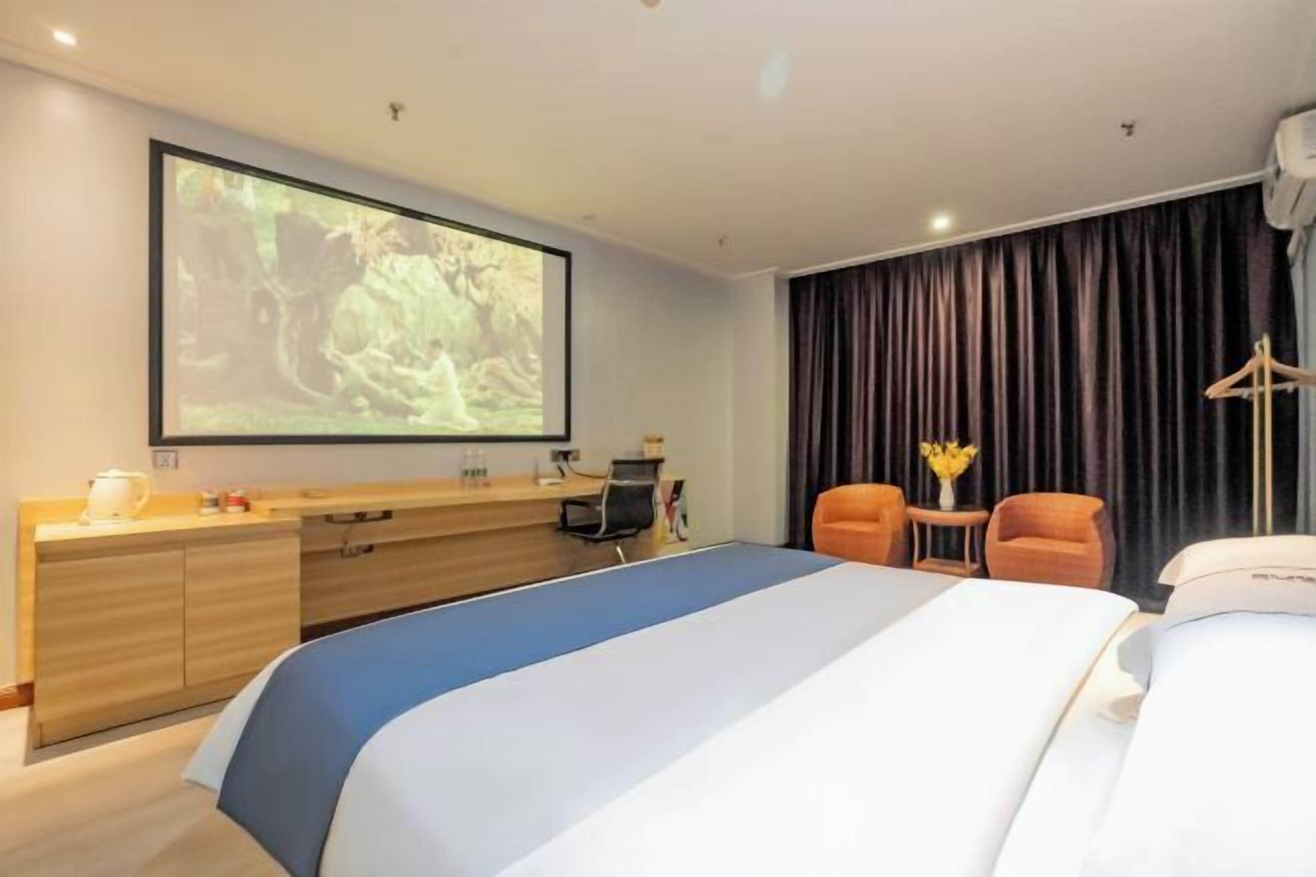 Habitación de hotel con cama, escritorio, silla, televisor y ventana con cortinas.